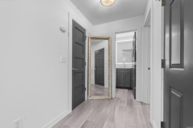 hallway featuring light wood-type flooring, baseboards, and a sink