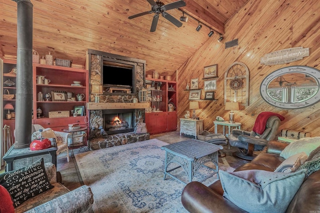living area with wood walls, track lighting, a wood stove, visible vents, and ceiling fan