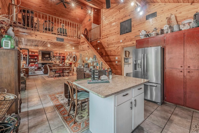kitchen with high vaulted ceiling, light tile patterned floors, wood walls, and stainless steel fridge