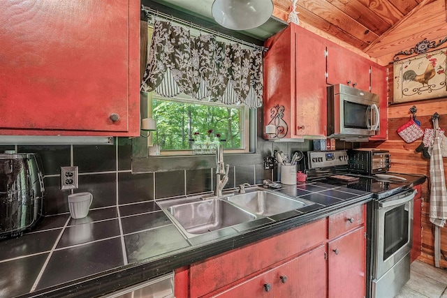 kitchen with backsplash, dark countertops, vaulted ceiling, a sink, and appliances with stainless steel finishes