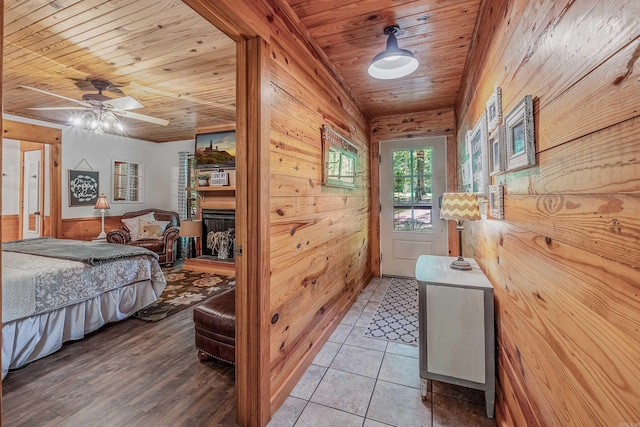 bedroom featuring a ceiling fan, a fireplace with raised hearth, light tile patterned floors, wood ceiling, and wood walls