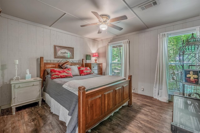 bedroom featuring ceiling fan, dark wood finished floors, wooden walls, and visible vents