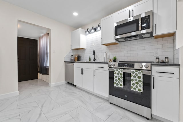 kitchen featuring white cabinets, a sink, appliances with stainless steel finishes, dark countertops, and baseboards