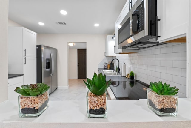 kitchen featuring white cabinetry, decorative backsplash, a sink, appliances with stainless steel finishes, and visible vents