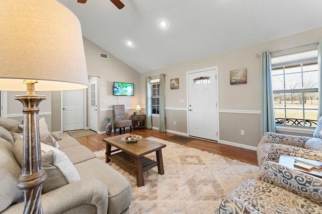 living room featuring visible vents, baseboards, wood finished floors, a ceiling fan, and high vaulted ceiling