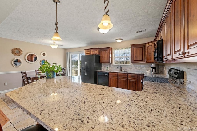 kitchen with black appliances, a peninsula, light stone counters, and plenty of natural light