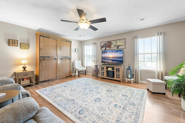 living room featuring a textured ceiling, ceiling fan, visible vents, and plenty of natural light