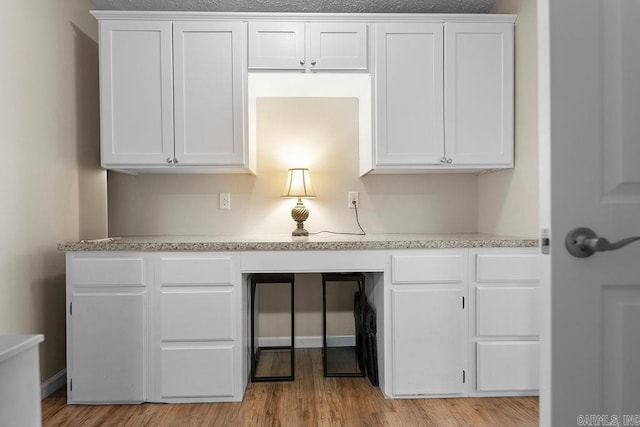 interior space featuring light wood finished floors, light stone countertops, and white cabinetry