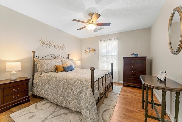 bedroom with a textured ceiling, a ceiling fan, light wood finished floors, and baseboards