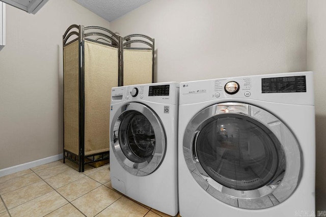 washroom with laundry area, light tile patterned floors, washing machine and clothes dryer, baseboards, and a textured ceiling