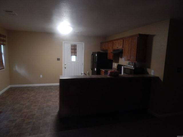 kitchen with stainless steel microwave, under cabinet range hood, a peninsula, baseboards, and freestanding refrigerator