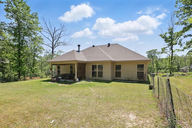 rear view of house featuring fence, roof with shingles, a lawn, and a hot tub