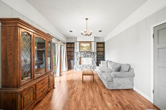 sitting room featuring a chandelier, a fireplace, light wood-type flooring, baseboards, and a textured ceiling