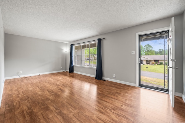 spare room featuring baseboards, wood finished floors, and a textured ceiling