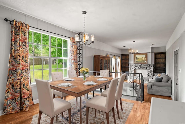 dining space with a stone fireplace, a wealth of natural light, a chandelier, and light wood-style floors