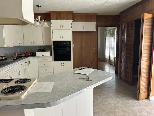 kitchen featuring under cabinet range hood, wood walls, white cooktop, black oven, and light floors