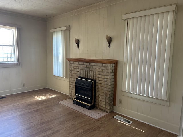 unfurnished living room featuring a brick fireplace, visible vents, baseboards, ornamental molding, and wood finished floors