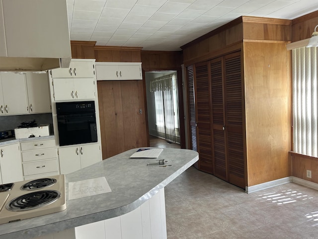 kitchen featuring light floors, oven, wood walls, electric stovetop, and range hood
