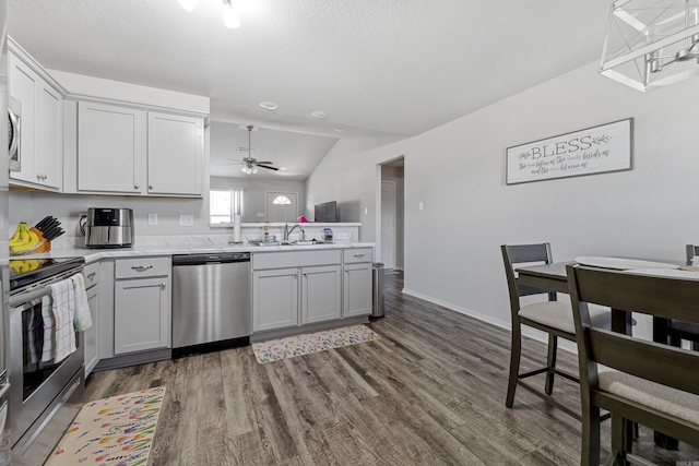 kitchen featuring appliances with stainless steel finishes, light countertops, dark wood finished floors, a peninsula, and gray cabinets