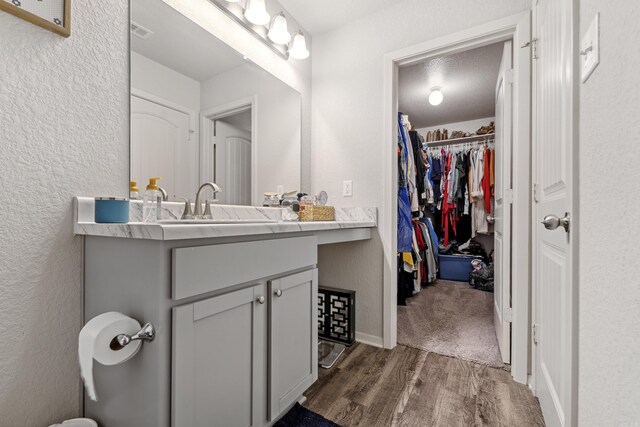 bathroom featuring a spacious closet, a textured wall, visible vents, wood finished floors, and vanity