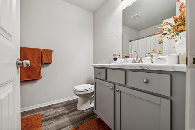 bathroom with wood finished floors, toilet, vanity, baseboards, and visible vents