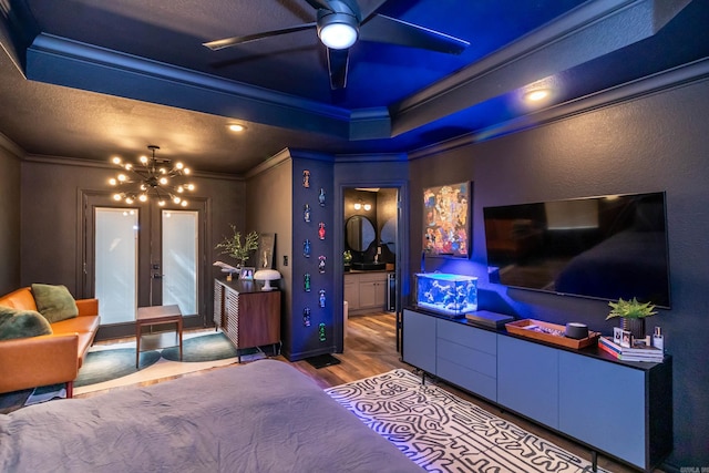 bedroom with crown molding, a raised ceiling, ensuite bathroom, wood finished floors, and a notable chandelier