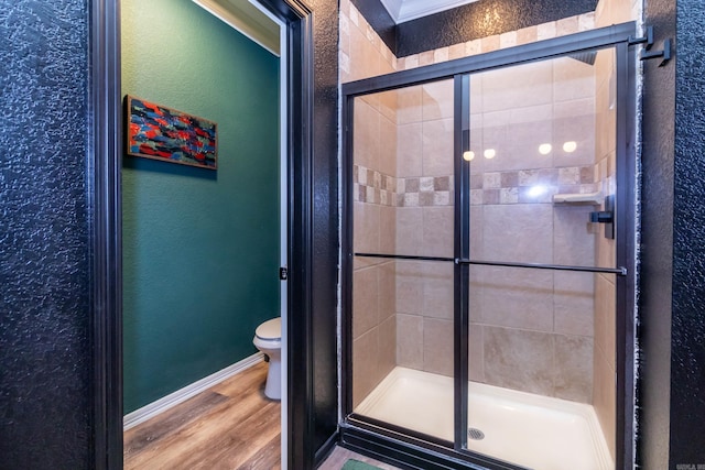full bath with wood finished floors, toilet, a textured wall, baseboards, and a stall shower