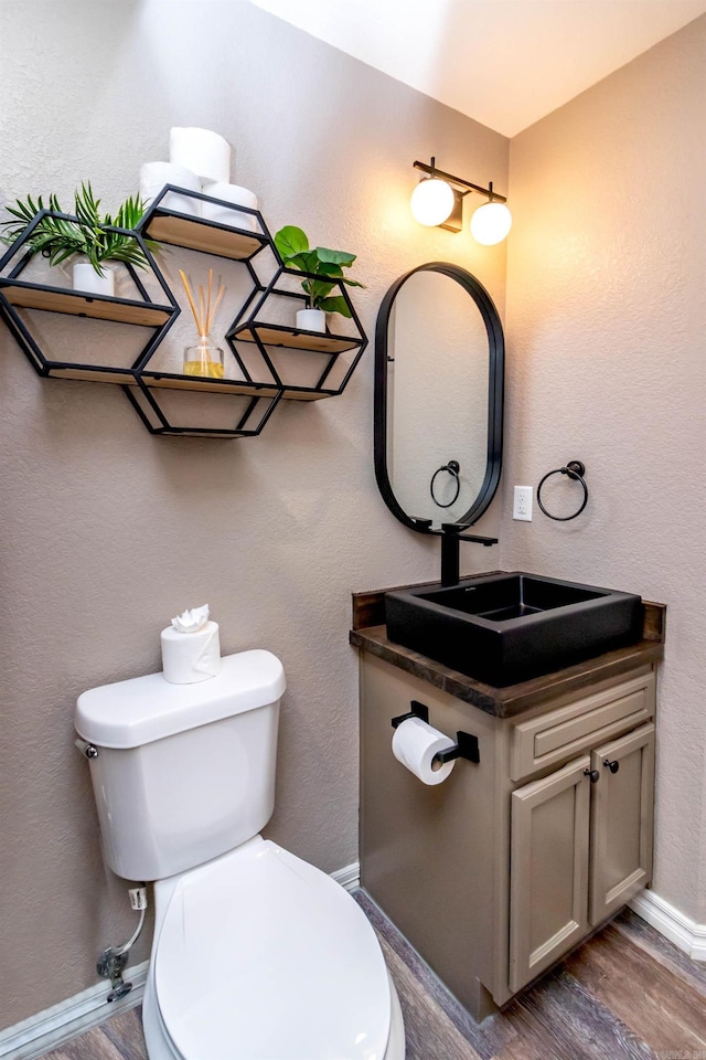 half bathroom with wood finished floors, toilet, a textured wall, and vanity