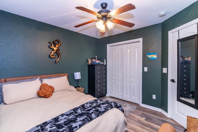 bedroom featuring wood finished floors, a closet, ceiling fan, a textured wall, and baseboards