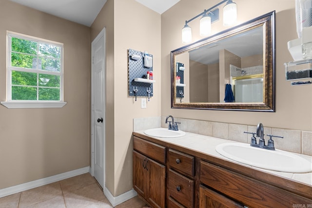 bathroom with a shower with shower door, double vanity, a sink, and baseboards