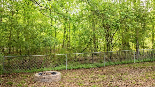 view of yard featuring a wooded view, a fire pit, and fence