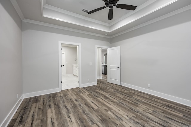 unfurnished bedroom with crown molding, baseboards, a raised ceiling, and dark wood finished floors