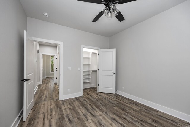 unfurnished bedroom with baseboards, ceiling fan, a walk in closet, and dark wood-style floors