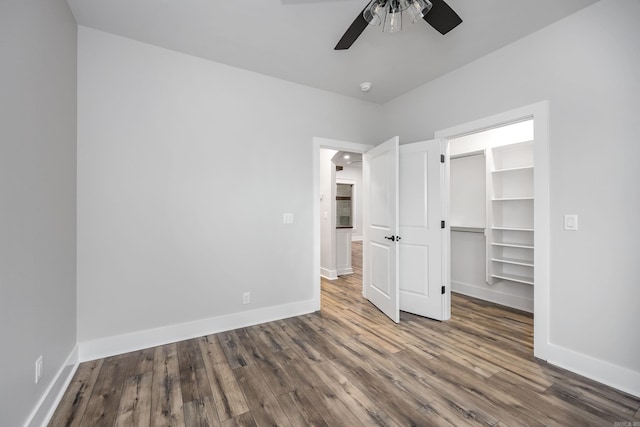 unfurnished bedroom with a closet, ceiling fan, a walk in closet, baseboards, and wood finished floors