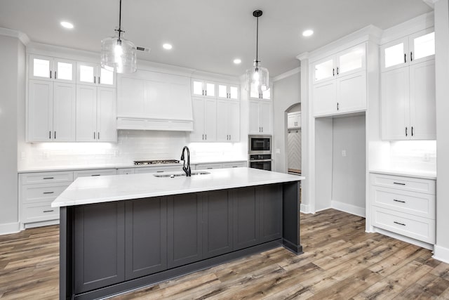 kitchen with a sink, stainless steel appliances, decorative backsplash, a center island with sink, and light countertops