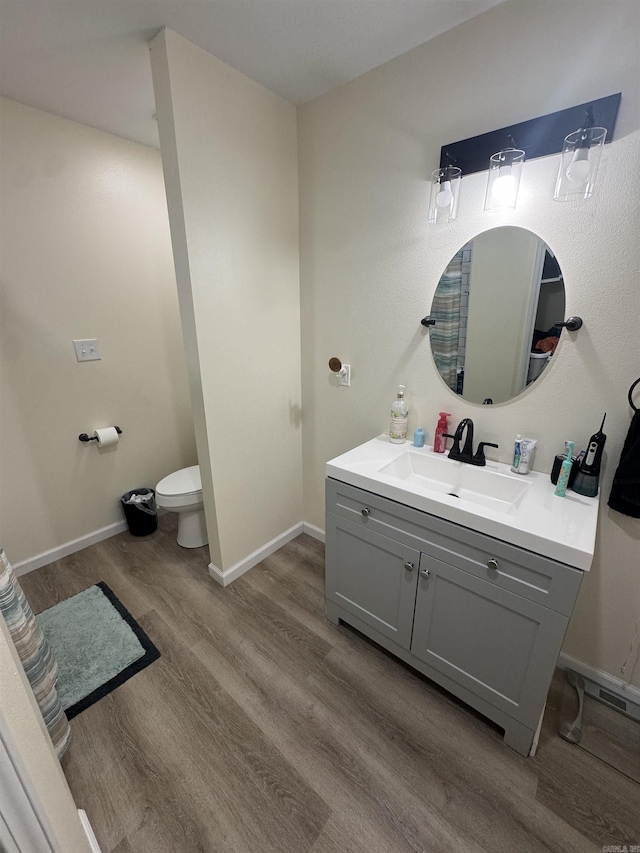 bathroom with toilet, vanity, wood finished floors, and baseboards