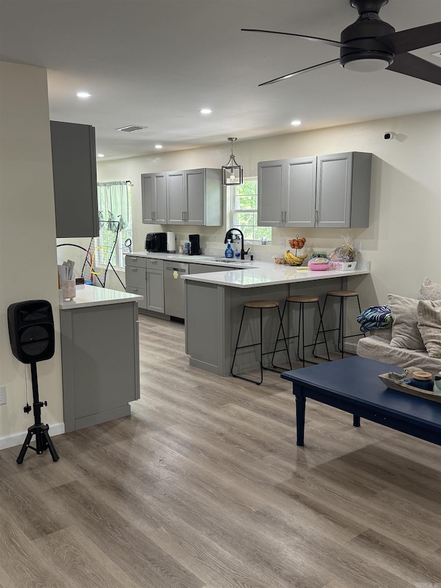 kitchen with gray cabinetry, a kitchen bar, light wood finished floors, and a peninsula
