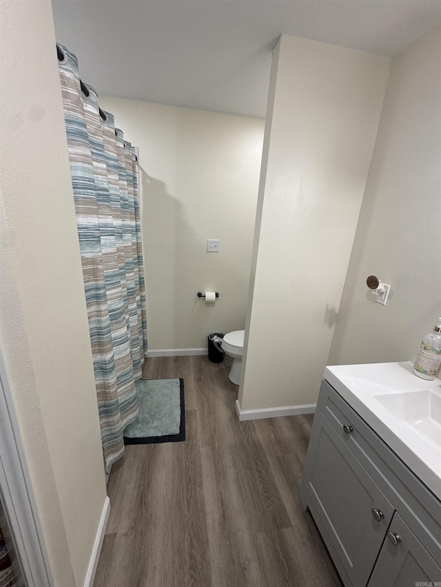 bathroom with a shower with curtain, baseboards, toilet, wood finished floors, and vanity
