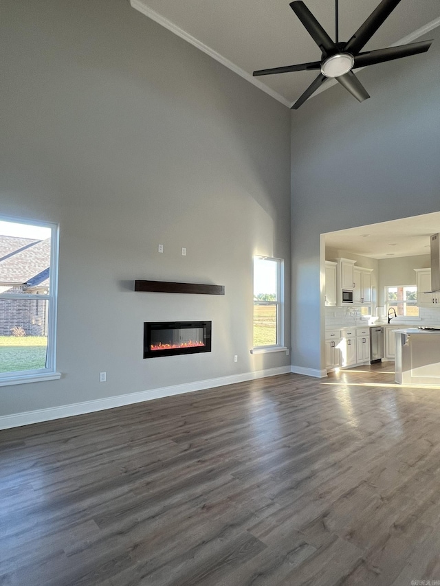 4406 Magee Dr, Texarkana, AR 71854 - unfurnished living room featuring a glass covered fireplace, dark wood-type flooring, a ceiling fan, baseboards, and a towering ceiling