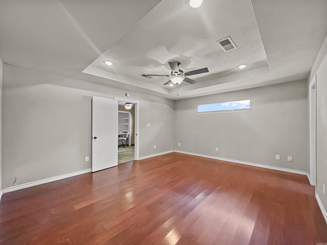 unfurnished bedroom with recessed lighting, a tray ceiling, visible vents, baseboards, and wood finished floors