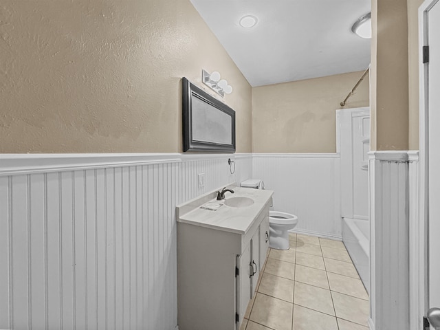 full bath with toilet, tile patterned floors, wainscoting, and vanity