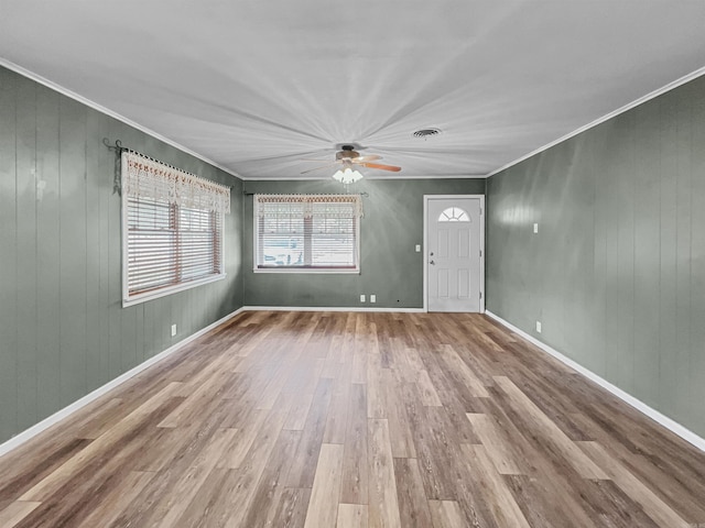 unfurnished living room with ceiling fan, wood walls, baseboards, ornamental molding, and wood finished floors
