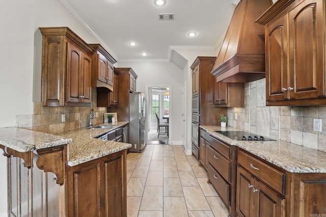 kitchen with a sink, custom range hood, a peninsula, light stone counters, and appliances with stainless steel finishes