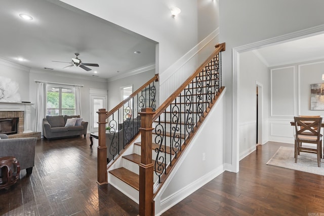 staircase featuring wood finished floors, ceiling fan, crown molding, and a brick fireplace