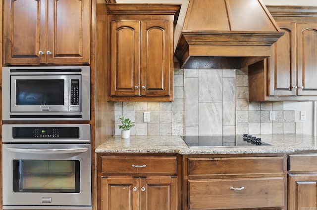 kitchen with light stone counters, custom exhaust hood, stainless steel appliances, and backsplash