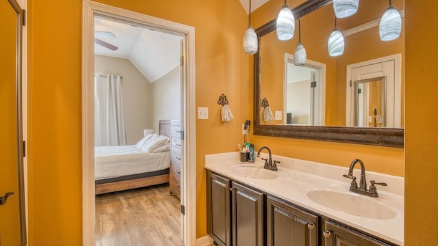 ensuite bathroom featuring wood finished floors, lofted ceiling, double vanity, and a sink