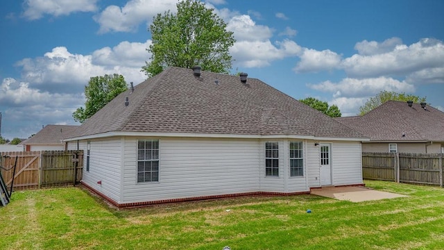 back of house featuring roof with shingles, a fenced backyard, and a lawn
