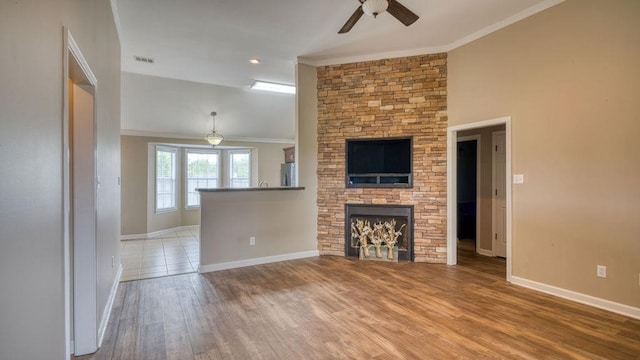 unfurnished living room with wood finished floors, ornamental molding, a fireplace, visible vents, and a ceiling fan