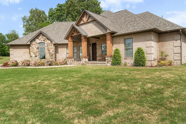 view of front of house with a front yard, stone siding, a shingled roof, and covered porch