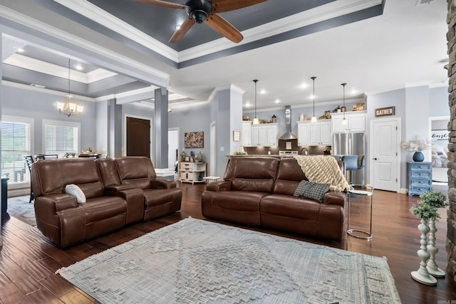living area featuring dark wood-style flooring, a raised ceiling, ornamental molding, and ceiling fan with notable chandelier